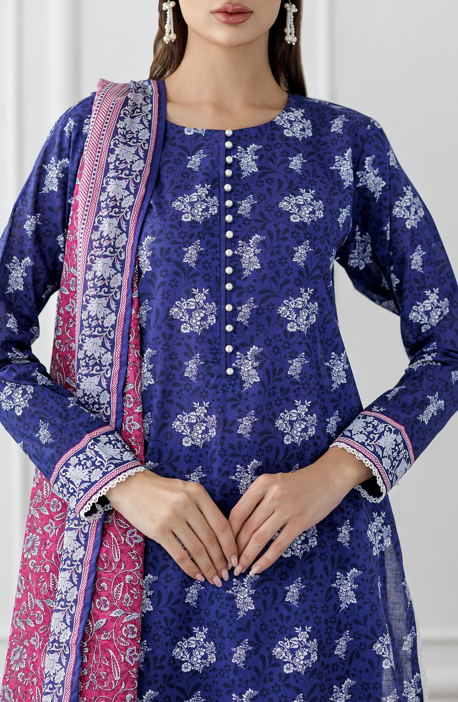 Woman wearing a blue floral dress with a pink dupatta against a plain trouser. Stitched Printed Lawn Shirt Dupatta & Pant - 3 Piece Suits - OTL-25-476