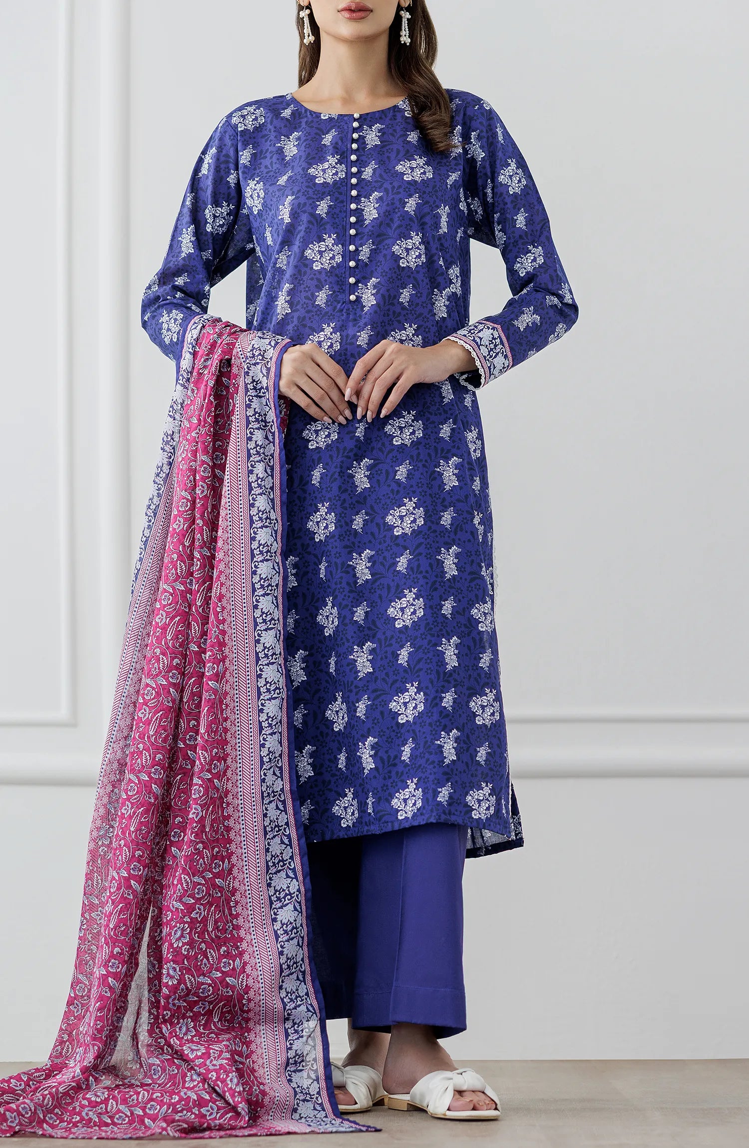 Woman wearing a blue floral dress with a pink dupatta against a plain trouser. Stitched Printed Lawn Shirt Dupatta & Pant - 3 Piece Suits - OTL-25-476