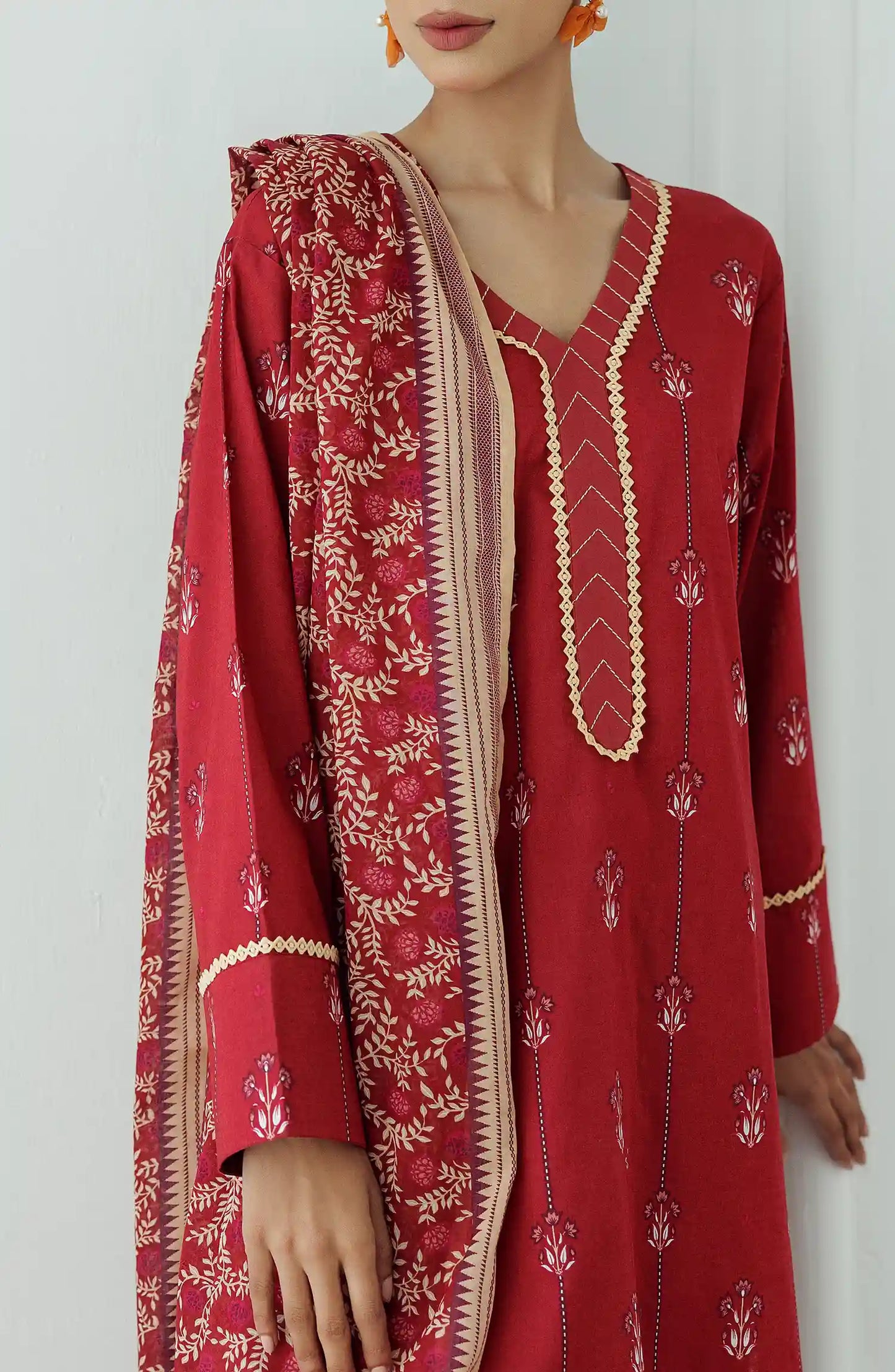 Women wearing a red printed traditional outfit with a matching dupatta on a white classic tapered shalwar at the hem. Stitched Printed Lawn Shirt Dupatta & Pant - 3 Piece Suits - OTL-25-066