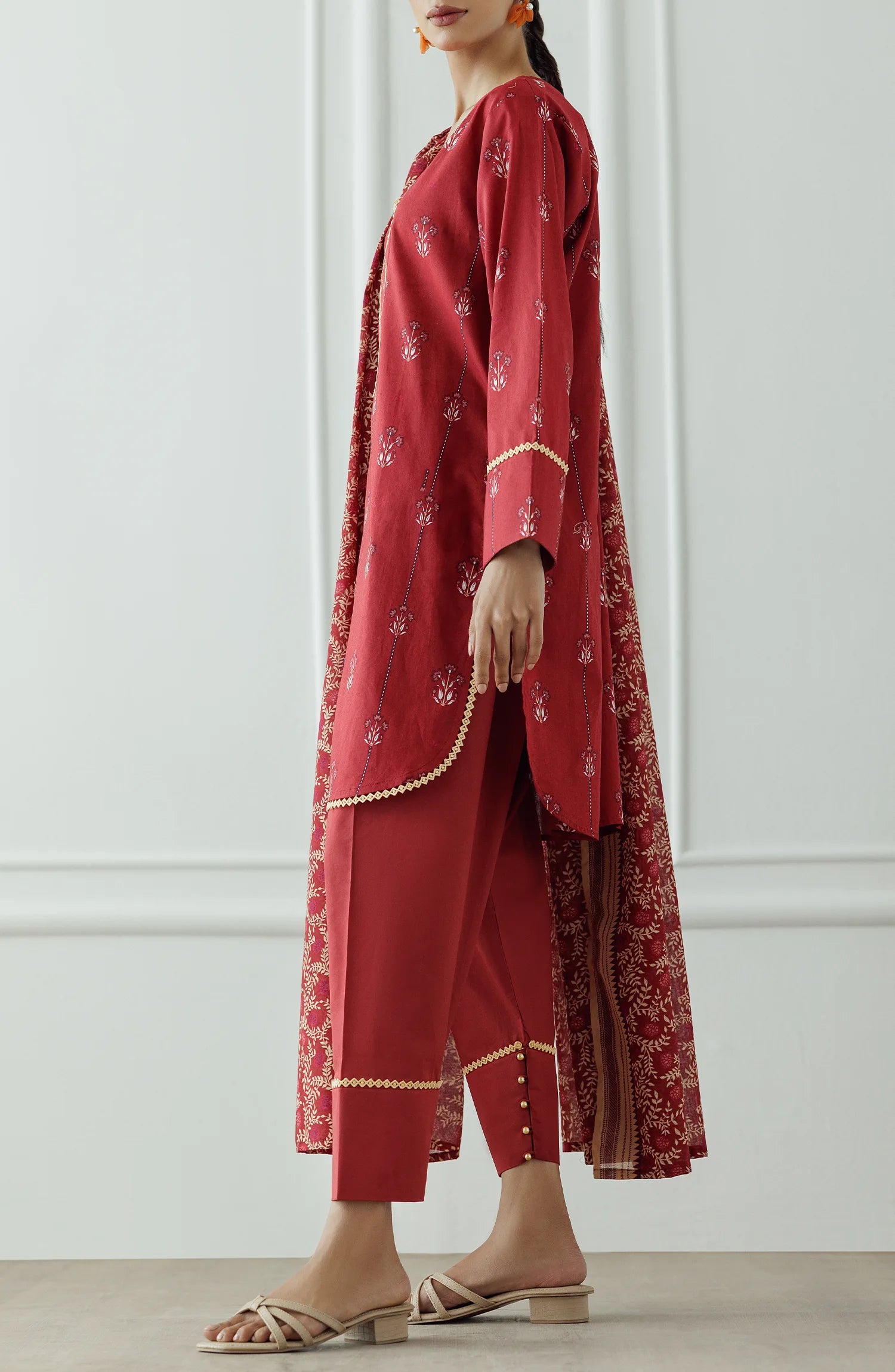 Women wearing a red printed traditional outfit with a matching dupatta on a white classic tapered shalwar at the hem. Stitched Printed Lawn Shirt Dupatta & Pant - 3 Piece Suits - OTL-25-066