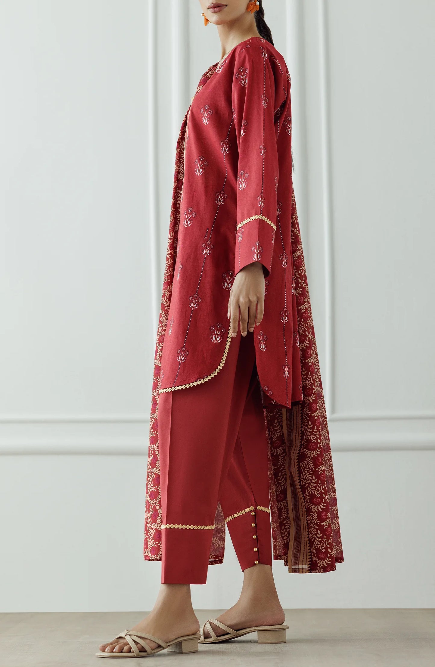 Women wearing a red printed traditional outfit with a matching dupatta on a white classic tapered shalwar at the hem. Stitched Printed Lawn Shirt Dupatta & Pant - 3 Piece Suits - OTL-25-066