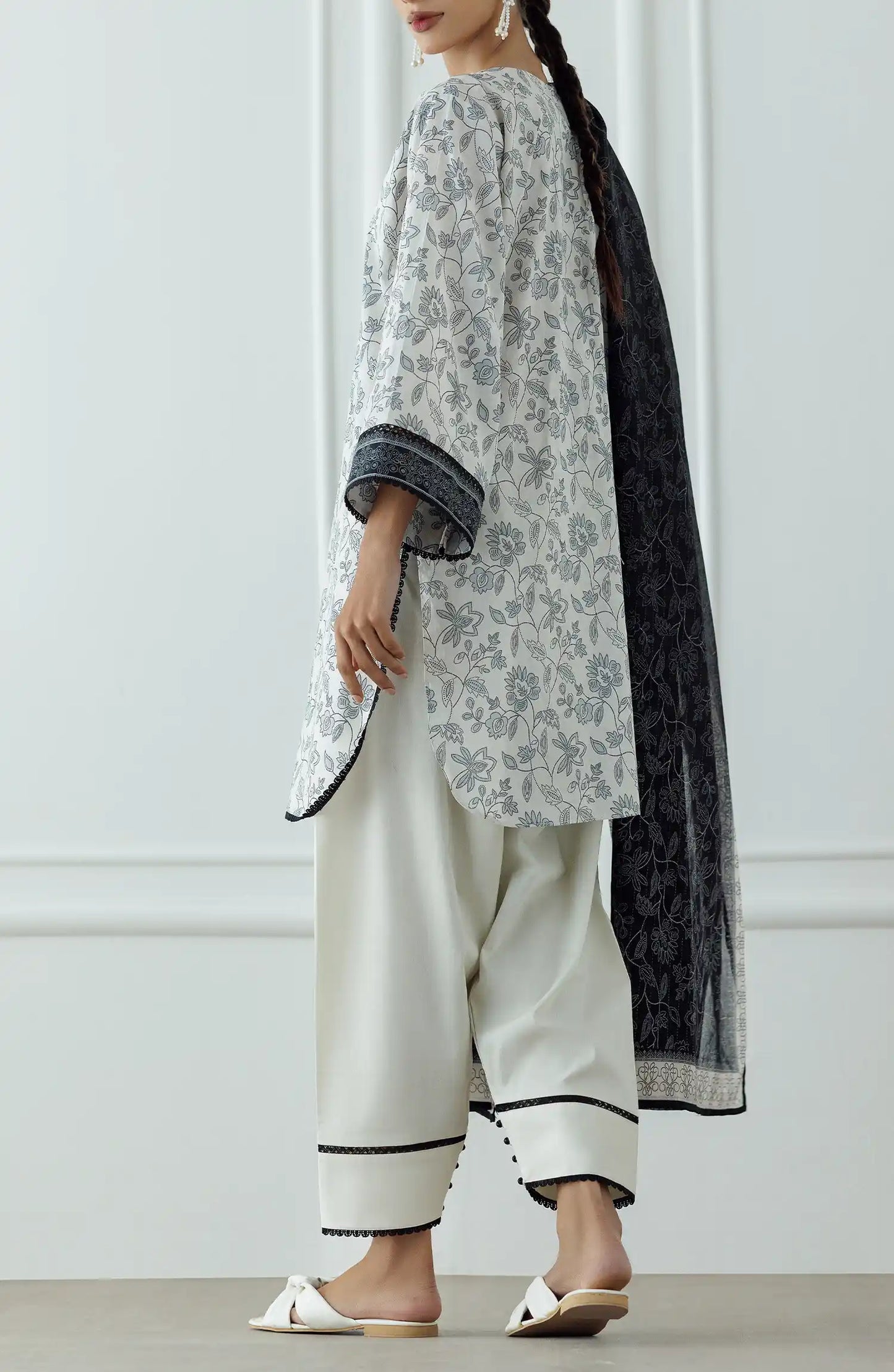 Woman wearing a traditional outfit with a white and gray patterned top and white pants against a traditional trouser. Stitched Printed Lawn Shirt Dupatta & Pant - 3 Piece Suits - OTL-25-336