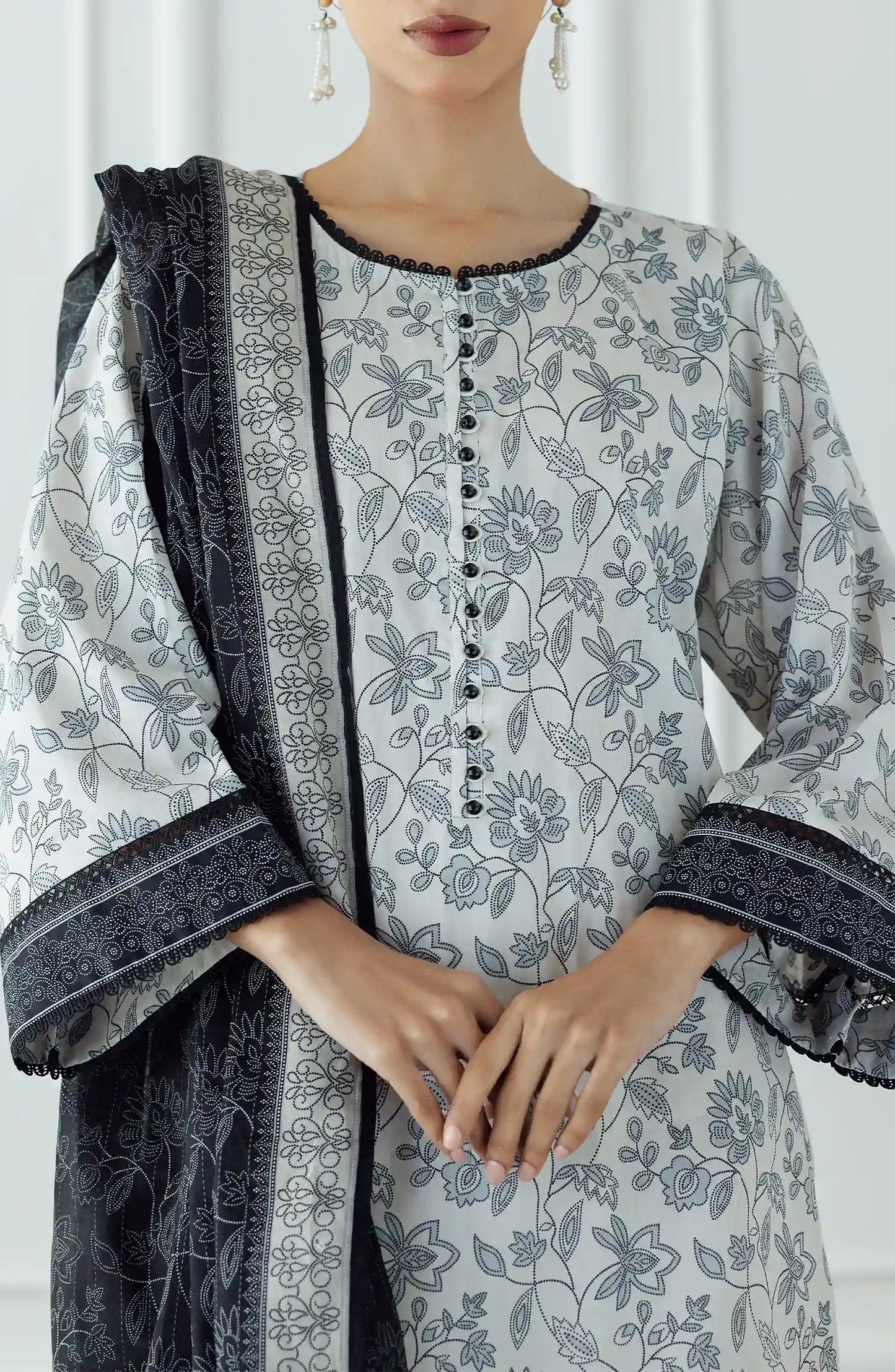 Woman wearing a traditional outfit with a white and gray patterned top and white pants against a traditional trouser. Stitched Printed Lawn Shirt Dupatta & Pant - 3 Piece Suits - OTL-25-336