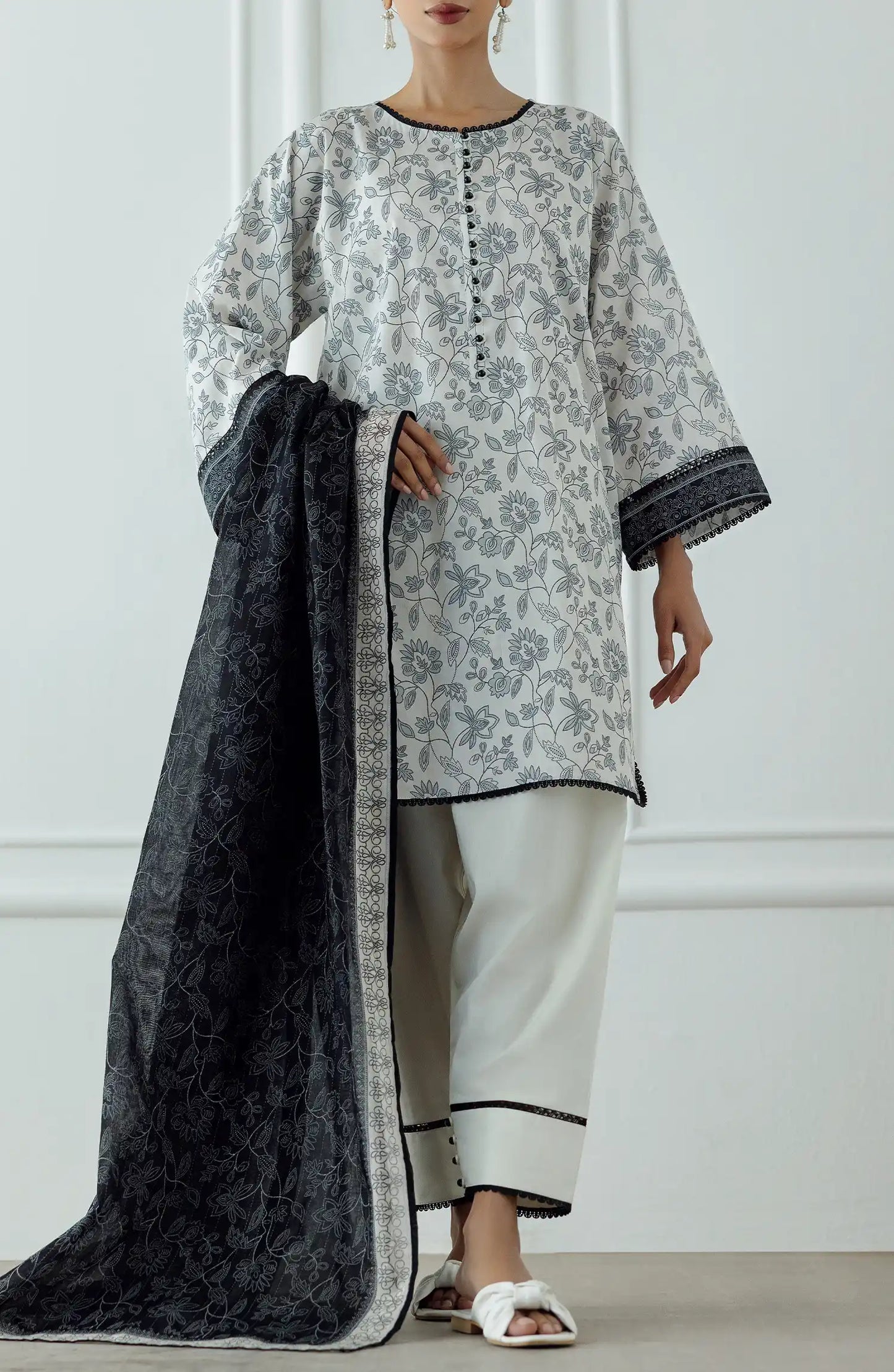 Woman wearing a traditional outfit with a white and gray patterned top and white pants against a traditional trouser. Stitched Printed Lawn Shirt Dupatta & Pant - 3 Piece Suits - OTL-25-336