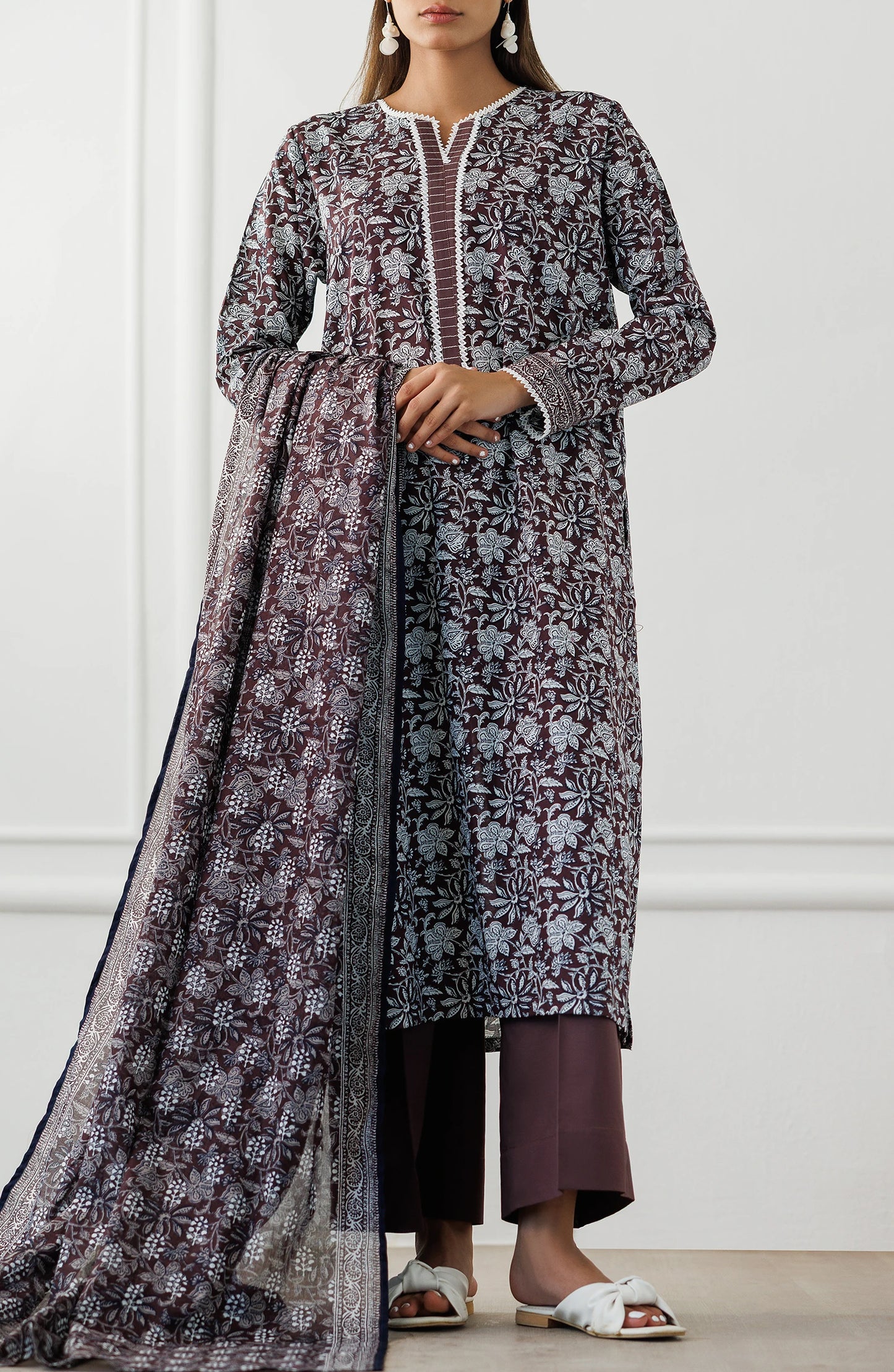 Woman wearing a long floral dress with a matching dupatta against a plain trouser. Stitched Printed Lawn Shirt Dupatta & Pant - 3 Piece Suits - OTL-25-371